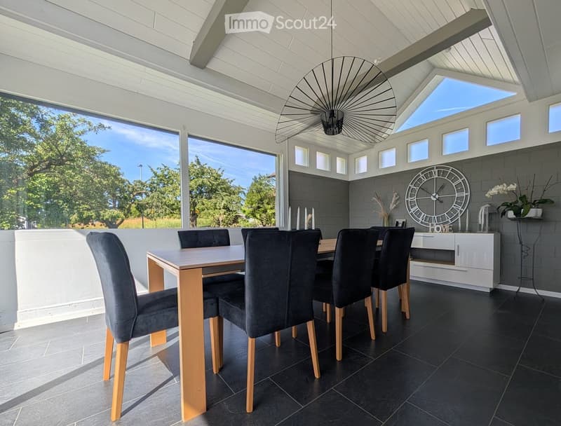 Modern dining room with a sleek wooden dining table, grey upholstered chairs, a white cabinet, a large wall clock, and decorative vases.