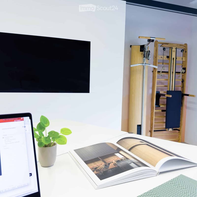 Furnished Room. A modern, well-lit room with a laptop, a potted plant, an open book, and a piece of fitness equipment in the background.