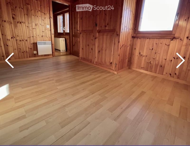 Unfurnished Room. Empty room with wooden walls and polished wooden flooring, featuring a radiator and a doorway leading to another room.