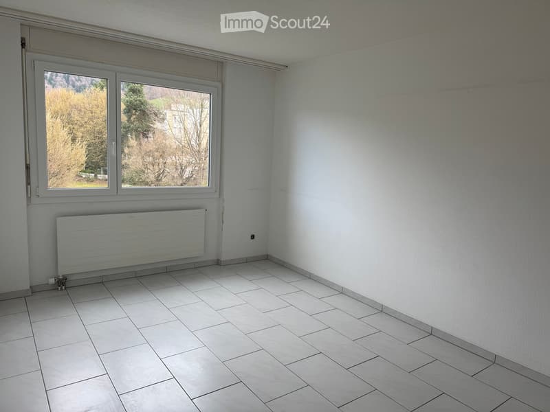 Unfurnished Room. Empty room with white tiled floor, white walls, large window with view of trees, and a radiator below the window.