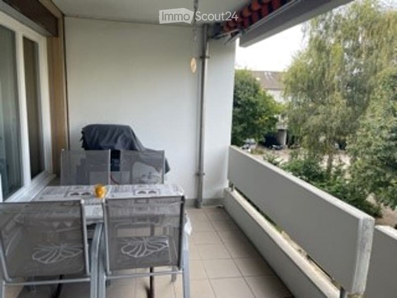 Balcony / Terrace. Balcony with tiled floor, white railing, outdoor table and chairs, umbrella, and view of greenery.