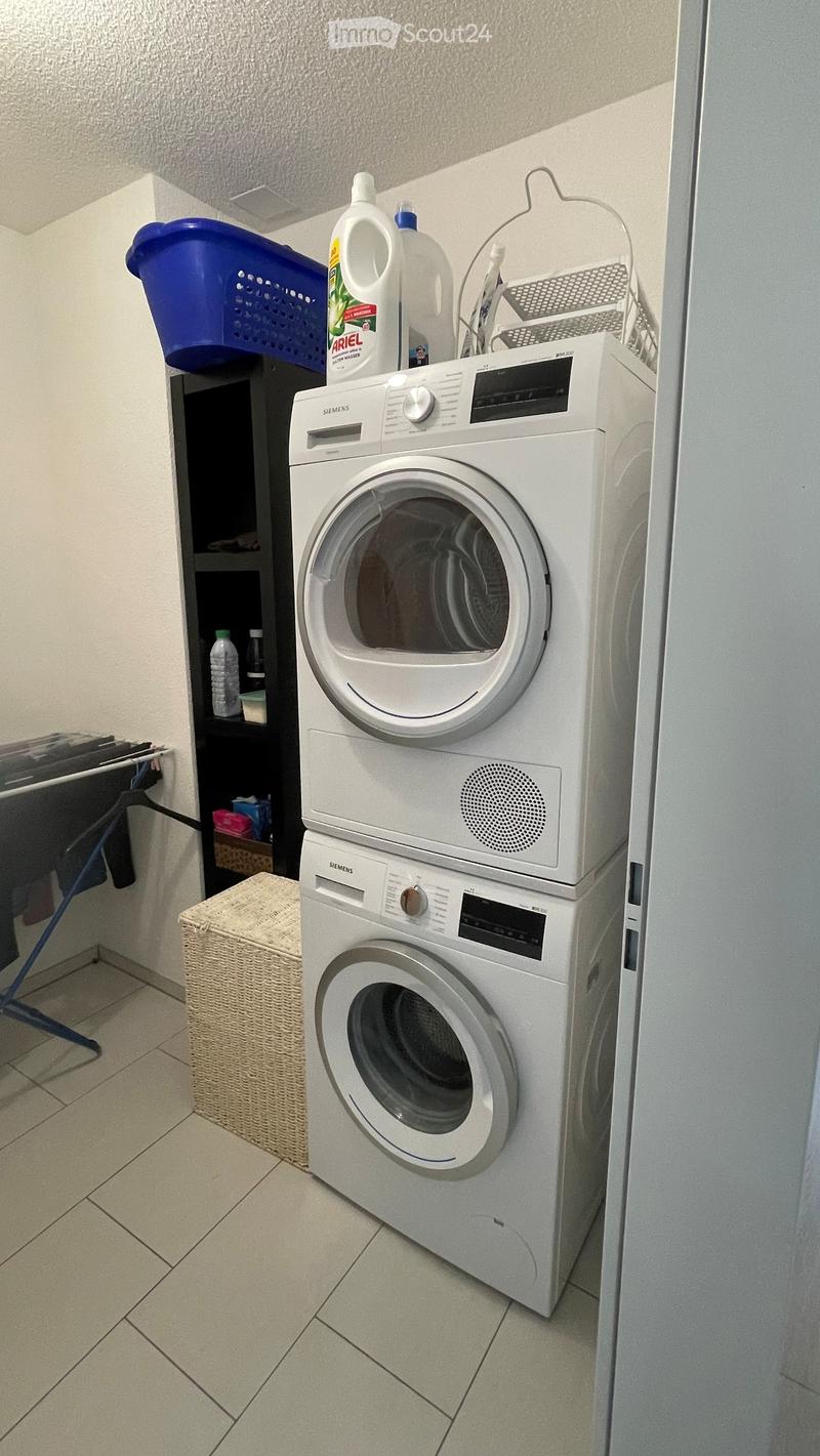 Stacked washing machine and dryer, black shelf, blue basket, wicker basket, clothes hanger, detergent bottles
