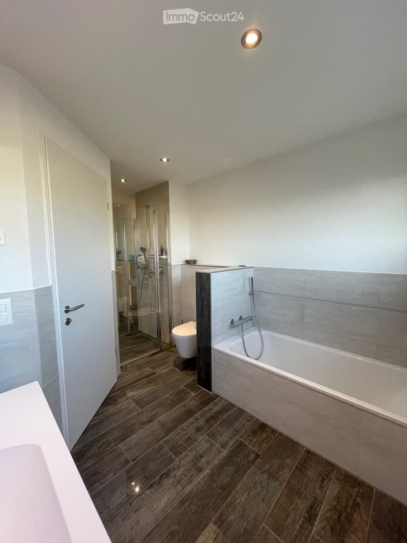 modern bathroom with wooden floor, white bathtub, glass shower enclosure, white toilet, white sink