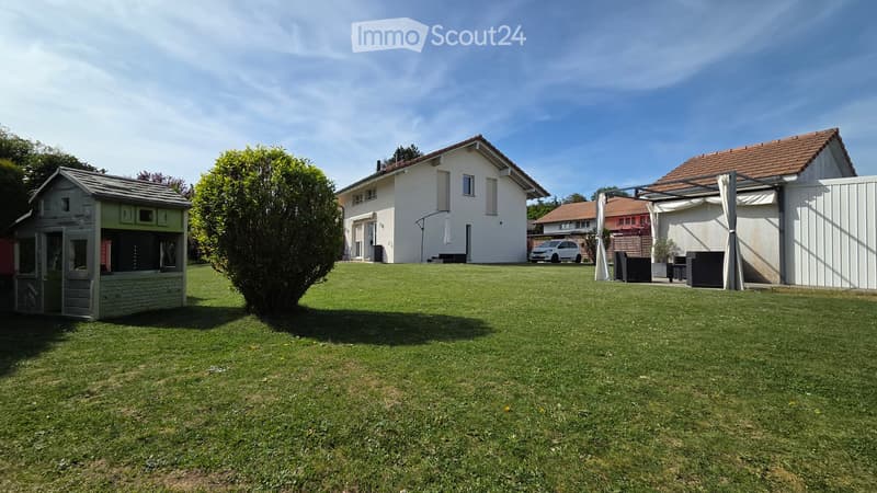 Garden / Outdoor Area. Well-maintained lawn with a playhouse, a large tree, and a white car parked near a house with a covered patio area.