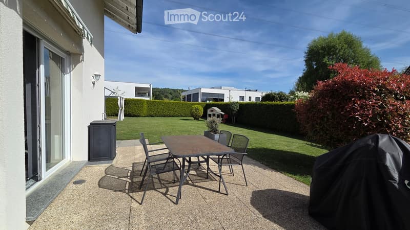 Garden / Outdoor Area. Outdoor patio with a table and chairs, covered barbecue, and a well-maintained lawn with hedges and trees.