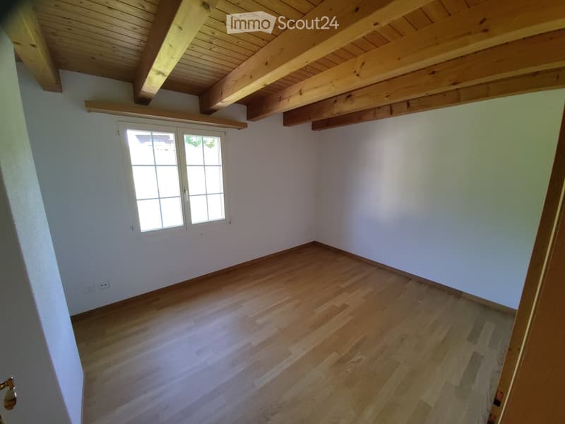 Unfurnished Room. Empty room with wooden flooring, white walls, and exposed wooden beams on the ceiling. A single window with white frames is visible on one wall.