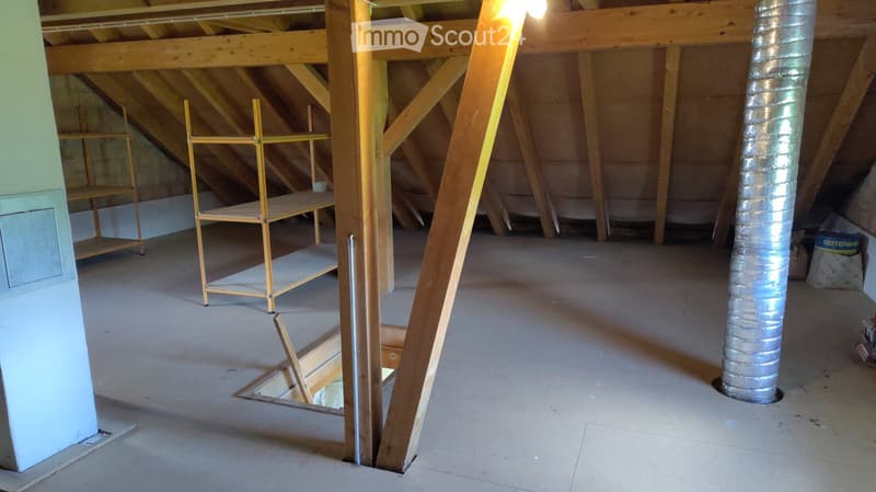 Unfurnished Room. Empty attic space with exposed wooden beams, concrete floor, and insulation ductwork. Scaffolding and storage shelves are present but no furniture.