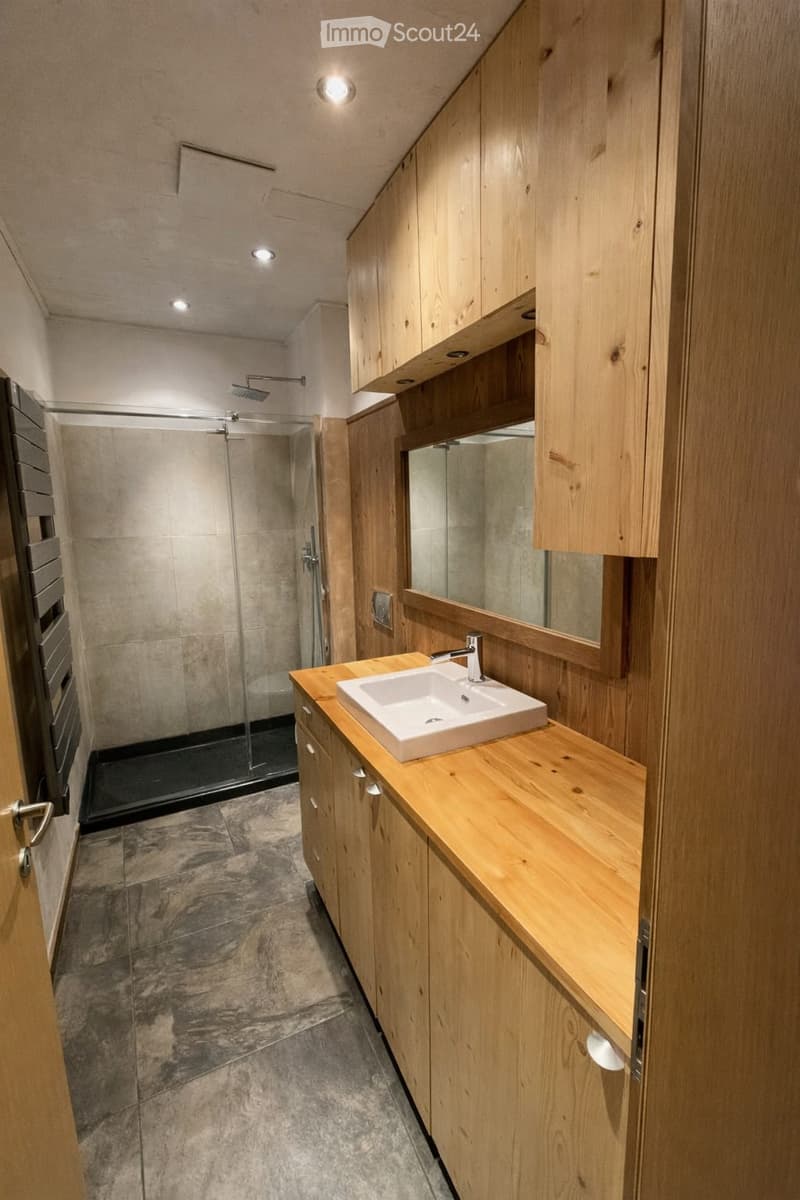 Bathroom. Modern bathroom with wooden cabinets, a white sink, a large mirror, and a glass-enclosed shower area.
