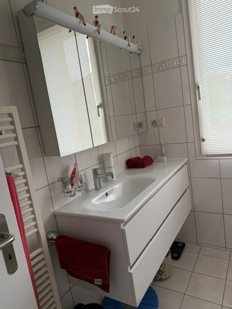 Bathroom. Modern bathroom with a white sink, large mirror, and red towels. The sink has a chrome faucet, and there are small decorative items on the counter.