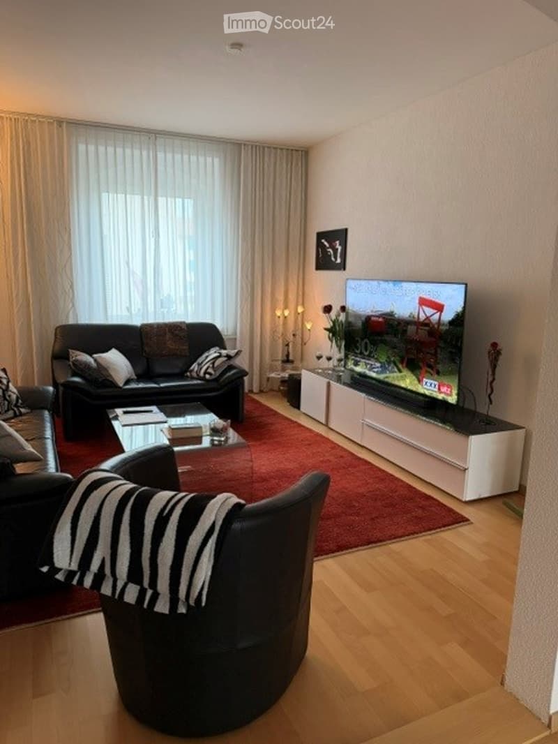 Living Room. Modern living room with a black leather sofa, coffee table, armchair, flat-screen TV, and decorative items on a side table.