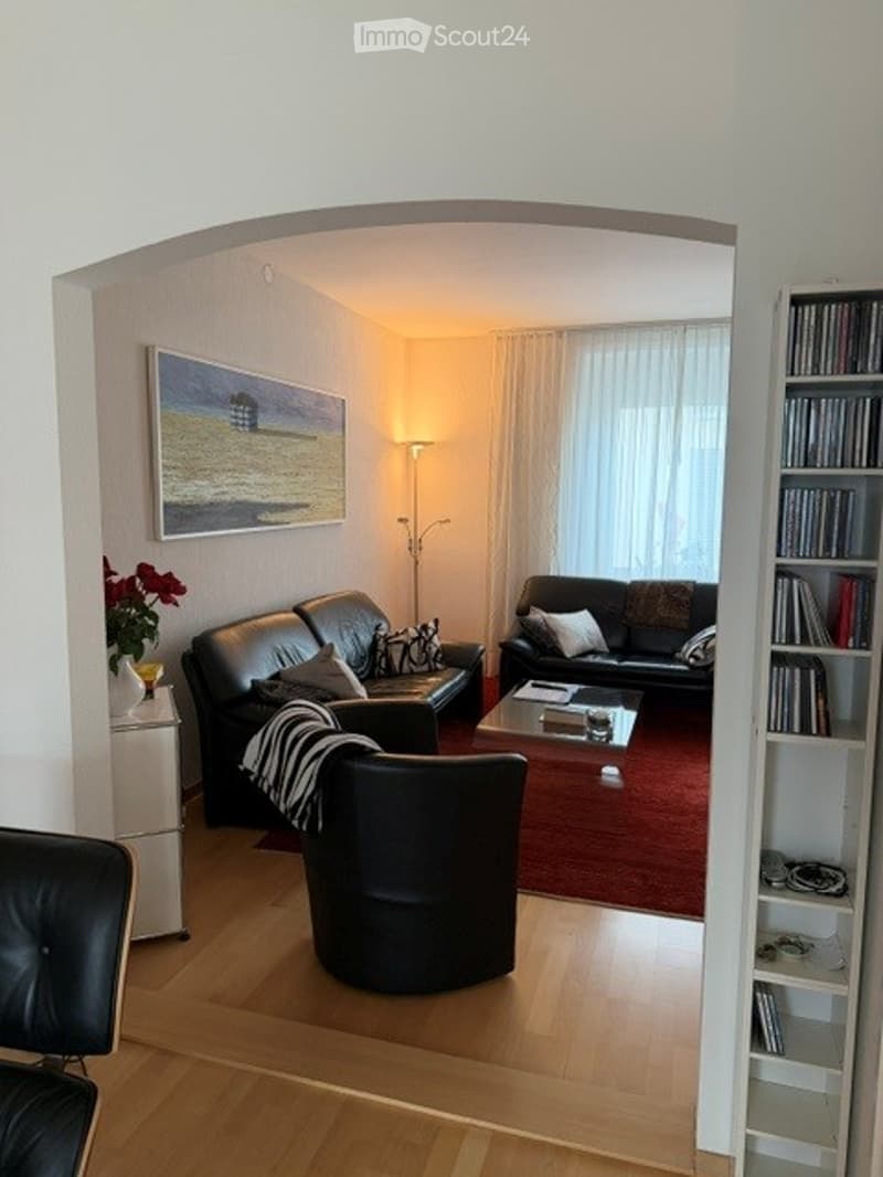 Living Room. Modern living room with dark leather sofas, a coffee table, an armchair, a floor lamp, a bookshelf, and a picture frame on the wall.