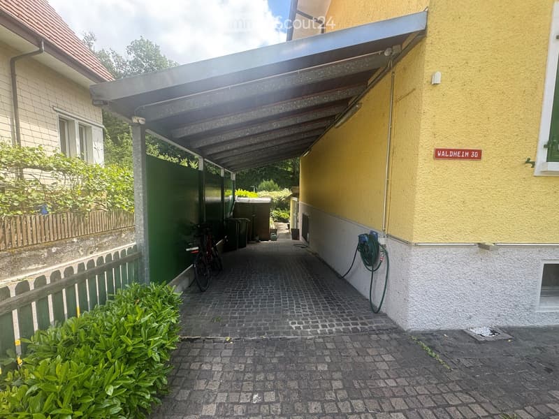 Corridor / Hallway. A covered outdoor corridor with brick pavement, green fence, bicycle, and garden area.