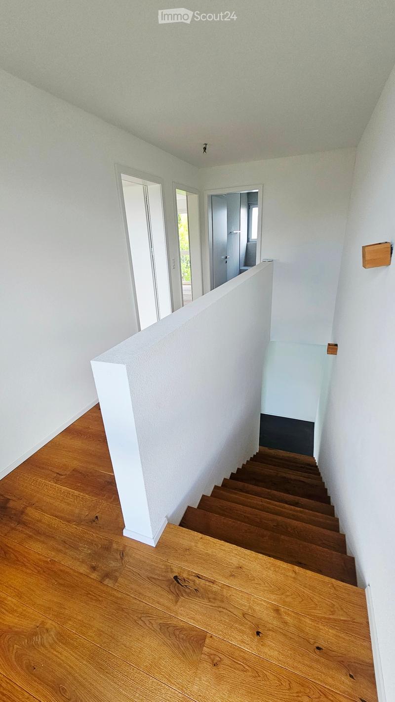 Corridor / Hallway. A modern hallway with wooden flooring, white walls, and a staircase leading upwards. The hallway features a white railing and several open doorways leading to other rooms.