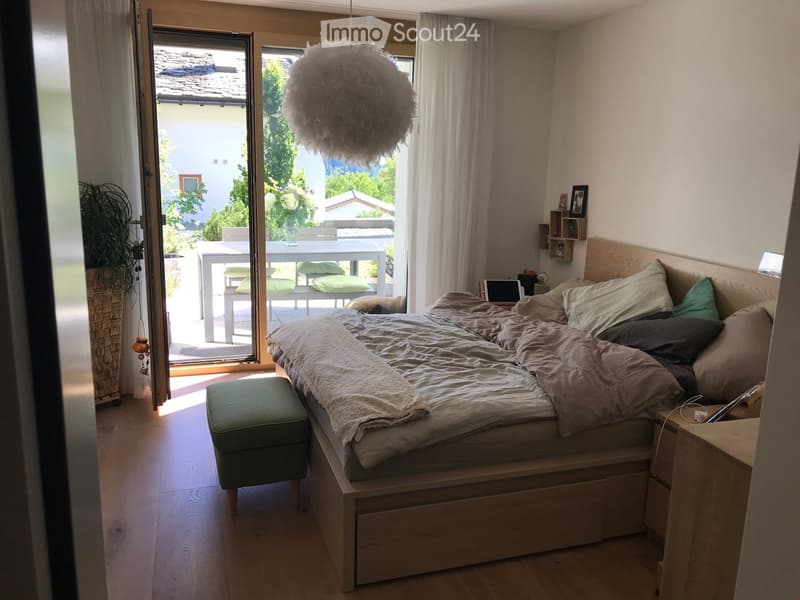 Bedroom. Cozy bedroom with a wooden bed, nightstand, green stool, and a view to a balcony with a table and chairs.