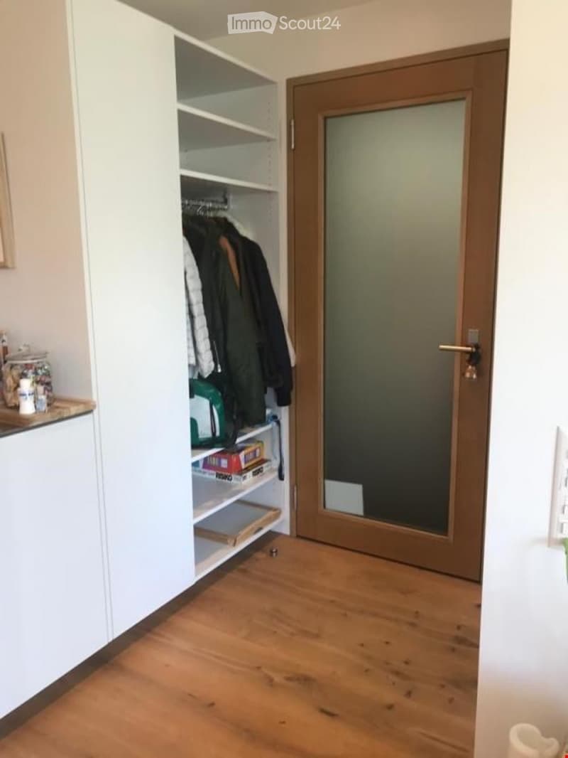 Furnished Room. A small, well-organized hallway with a built-in white wardrobe, coat rack, and shelves. The floor is wooden, and there is a partially visible kitchen counter on the left side.