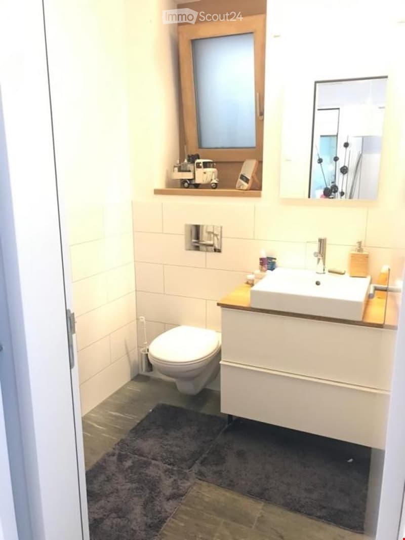 Bathroom. Modern bathroom with white tiles, a toilet, a sink with a mirror, and a small shelf above the window.