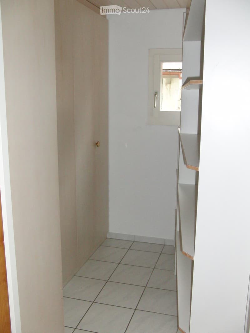 Corridor / Hallway. Empty hallway with tiled floor, white walls, and a small window at the end.
