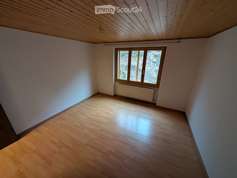 Unfurnished Room. Empty room with wooden flooring, white walls, and a large window with wooden frame. The ceiling is slanted with wooden beams.