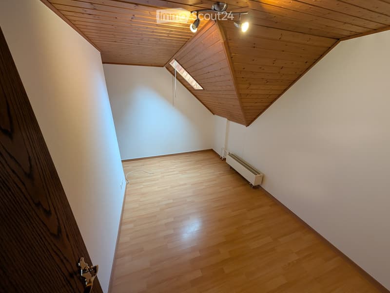 Unfurnished Room. Empty room with wooden flooring, white walls, and a slanted wooden ceiling. A small window allows natural light to enter, and a radiator is visible against one wall.