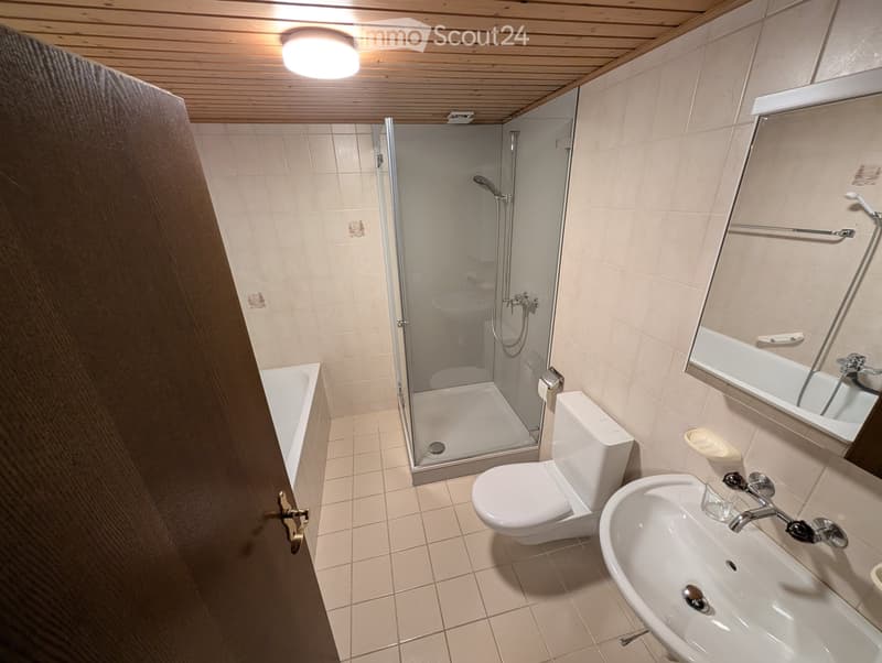 Bathroom. Modern bathroom with a white toilet, sink, bathtub, and glass-enclosed shower. Features tiled walls and a wooden ceiling with a central light fixture.