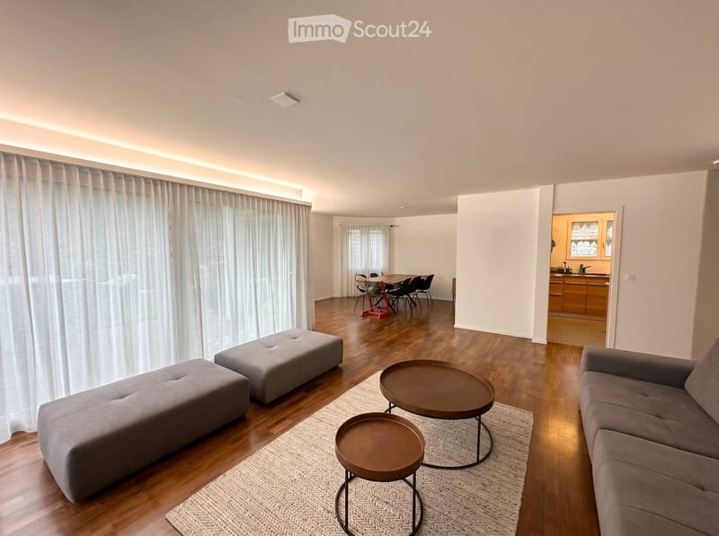 Furnished Room. Modern living room with grey sofa, wooden floor, round tables, and a dining area with chairs and a table.
