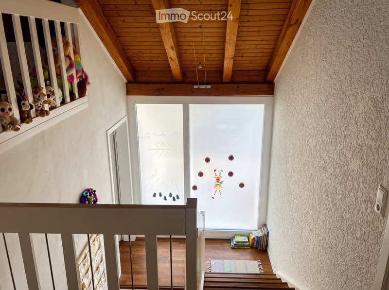 Corridor / Hallway. Staircase with wooden railings, plush toys on a shelf, books stacked on the floor, and a frosted glass door with festive decorations.