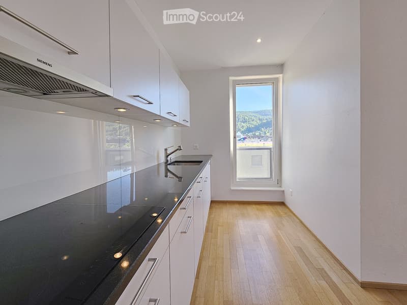 Kitchen. Modern kitchen with white cabinets, black countertop, stainless steel sink, and range hood. Large window offers a scenic view.