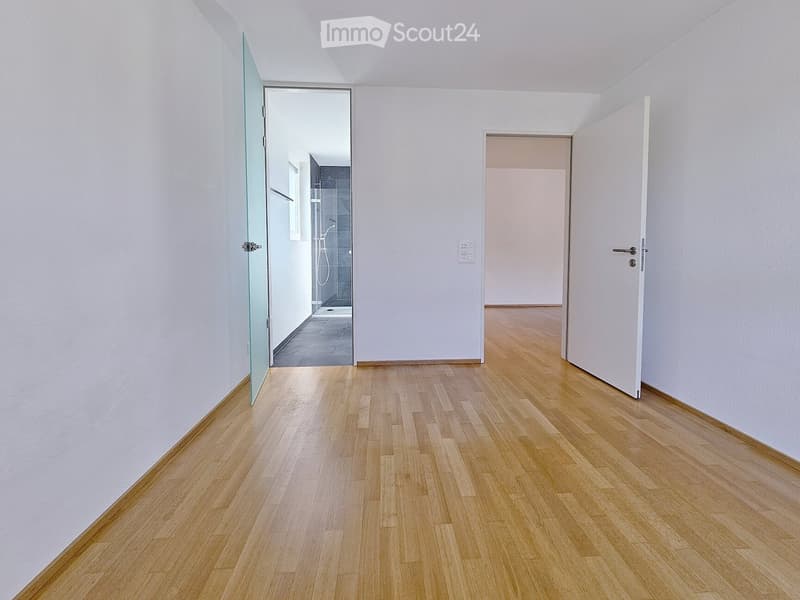 Corridor / Hallway. Empty hallway with light wooden flooring, white walls, and two open doors leading to other rooms.