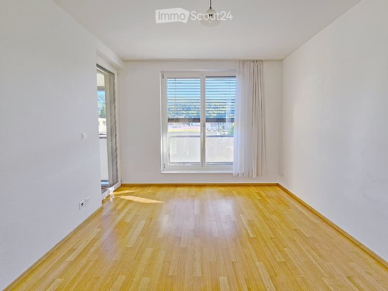 Unfurnished Room. Empty room with light wooden flooring, white walls, large window with blinds, and a sliding glass door leading to a balcony.