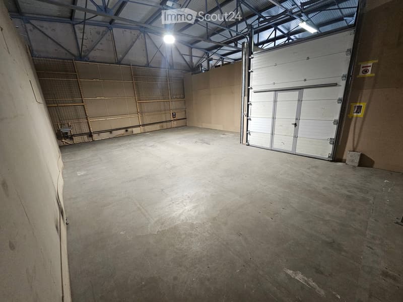 Unfurnished Room. Empty warehouse space with concrete floor, large garage door, and metal shelving units against the wall.