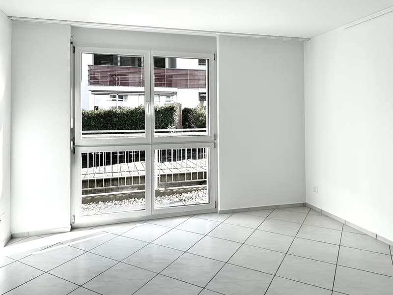 Empty room, white tiled floor, white walls, large glass sliding doors with metal railings, view to balcony