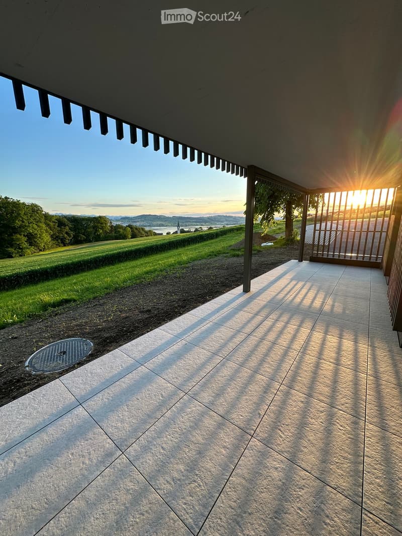 Balcony / Terrace. A covered outdoor patio with large stone tiles, overlooking a grassy field and distant landscape at sunset.