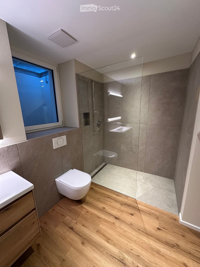 Bathroom. Modern bathroom with wooden flooring, a toilet, a sink, a glass-enclosed shower, and a large window with a view of the night sky.