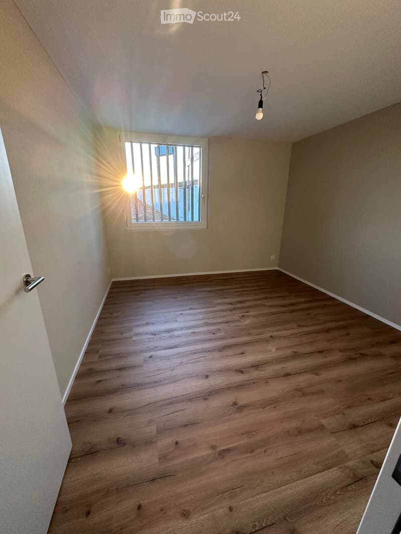 Unfurnished Room. Empty room with wooden flooring, white walls, and a single window with bars letting in natural light.