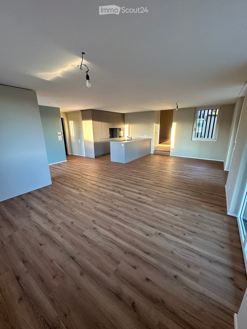 Unfurnished Room. Empty room with wooden flooring, white walls, and a small kitchen area visible in the background.