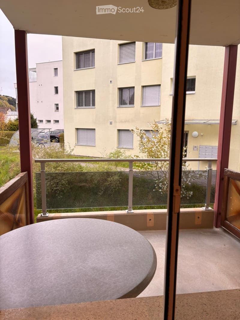 Balcony / Terrace. Balcony with a round table, metal railing, and view of a residential building and greenery.