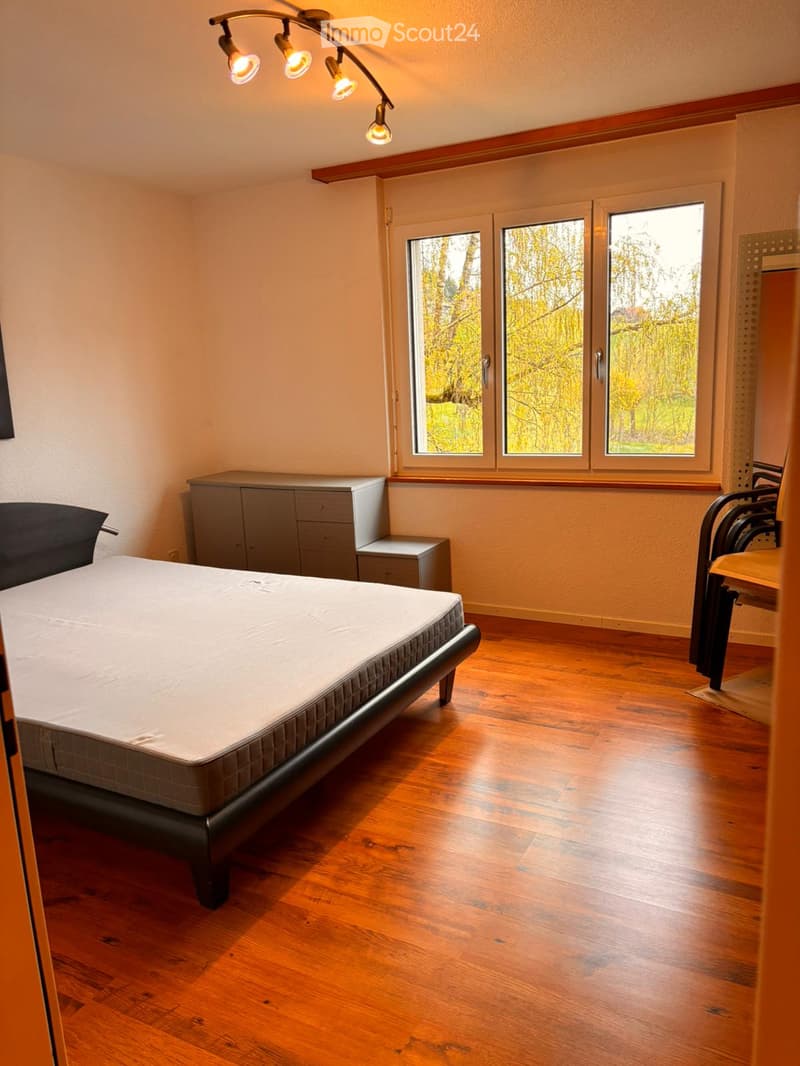 Bedroom. Spacious bedroom with wooden flooring, large windows, a double bed with a mattress, a cabinet, and a chair.