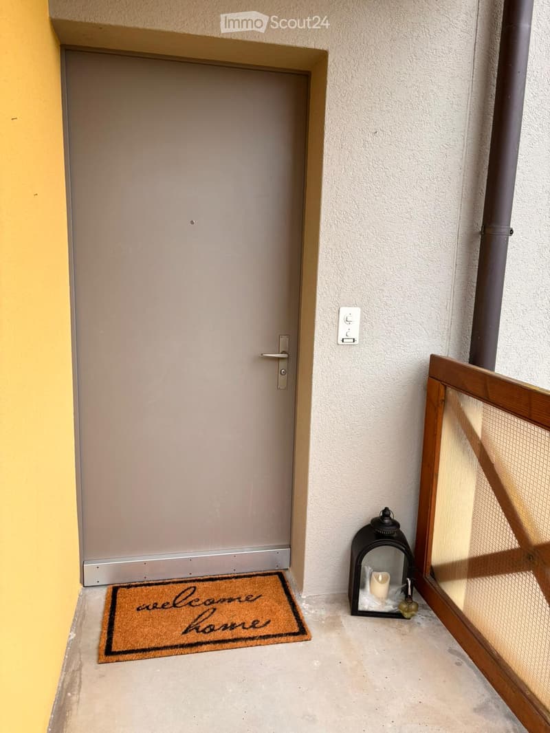 Corridor / Hallway. A small entryway with a door, a welcome mat, and a lantern with a candle on the floor.