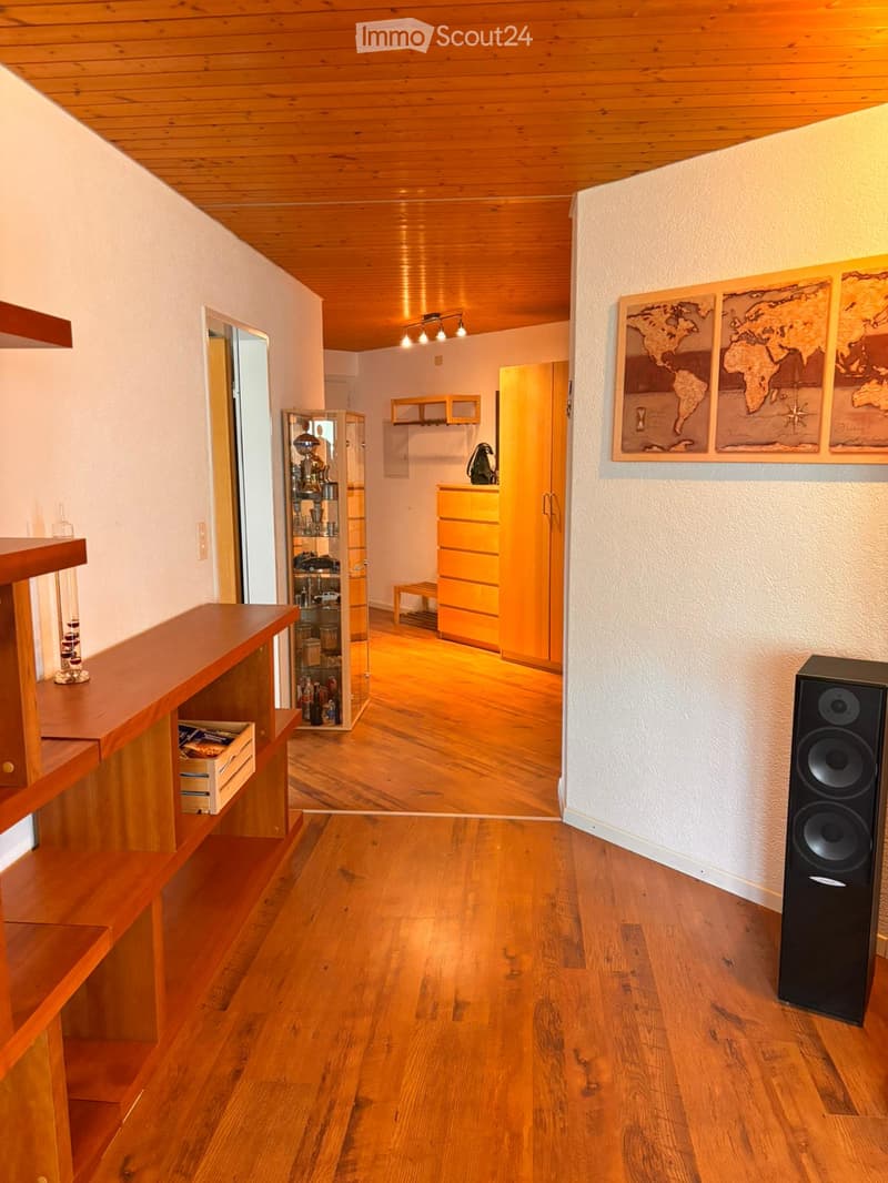 Furnished Room. A well-lit hallway with wooden flooring and a wooden ceiling, featuring a wooden shelf on the left, a large speaker on the right, a glass cabinet with trophies, and a world map on the wall.