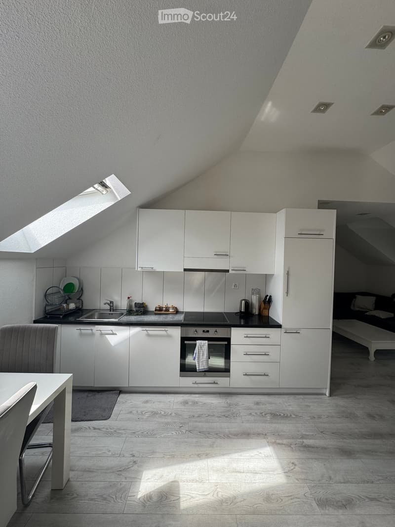 Kitchen. Modern kitchen with white cabinets, stainless steel appliances, and a black countertop. Features a built-in oven, sink, and a small dining area with a table and chair.