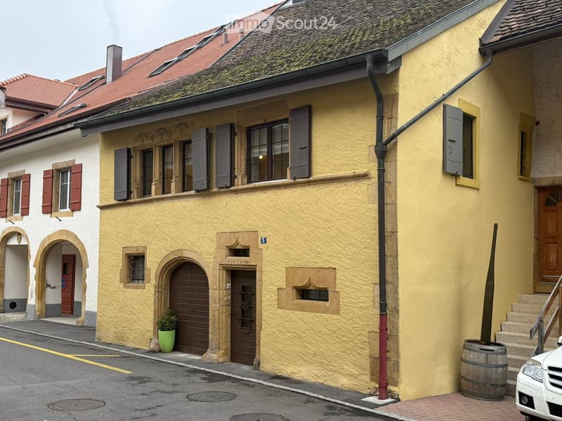 Building. Two-story building with yellow and white facades, red-tiled roof, multiple windows with shutters, arched doorways, and a small green plant in a pot near the entrance.