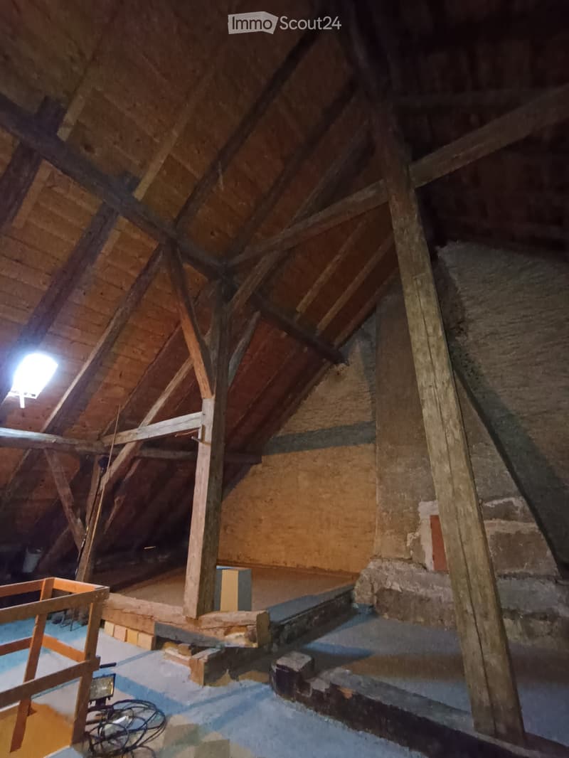 Unfurnished Room. An attic space with exposed wooden beams, insulation, and a partially finished floor. The area includes construction materials and tools, indicating ongoing renovation.