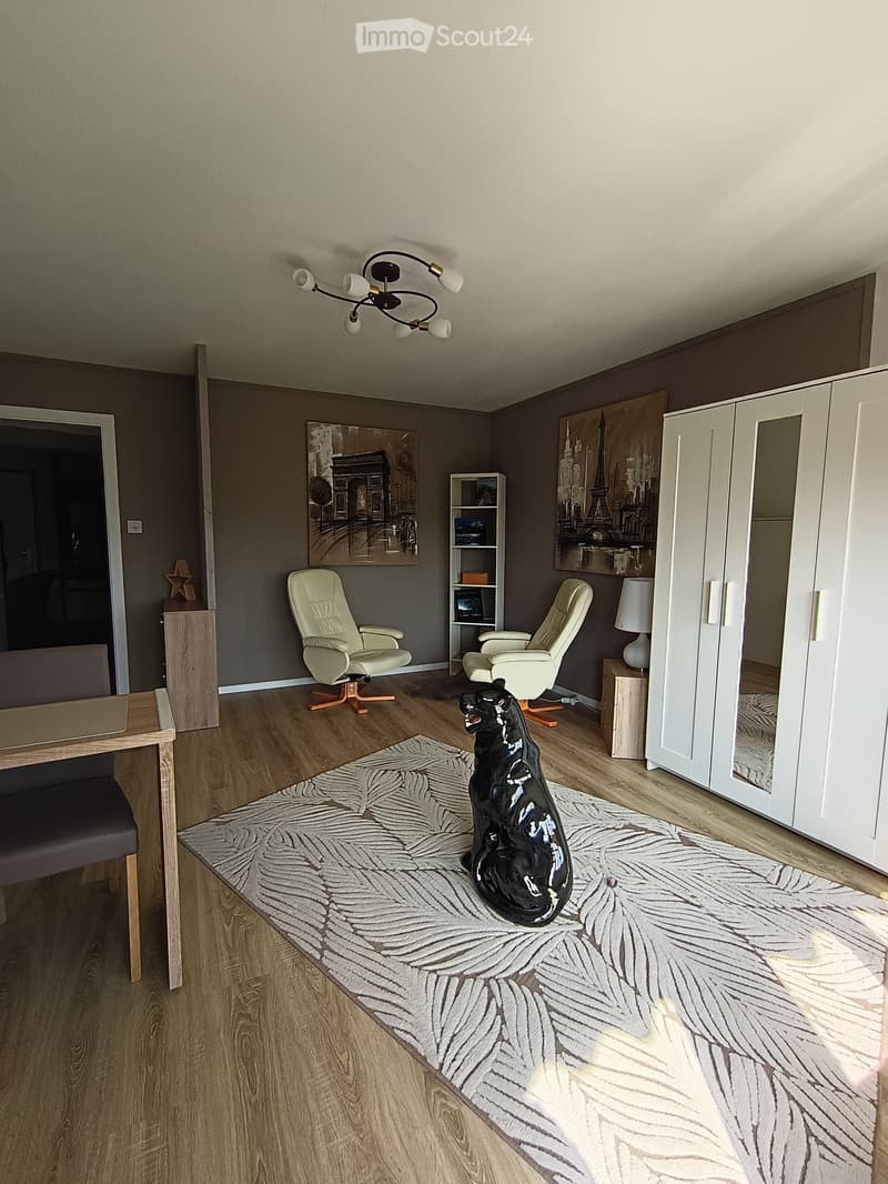 Furnished Room. Modern living room with wooden flooring, white cabinet, two white armchairs, a black statue on a rug, a shelf with books, and a table with a chair.