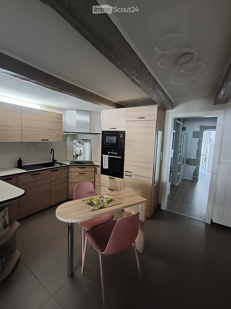 Kitchen. Modern kitchen with light wood cabinets, stainless steel appliances, a small round table with two pink chairs, and a sink area with a faucet.