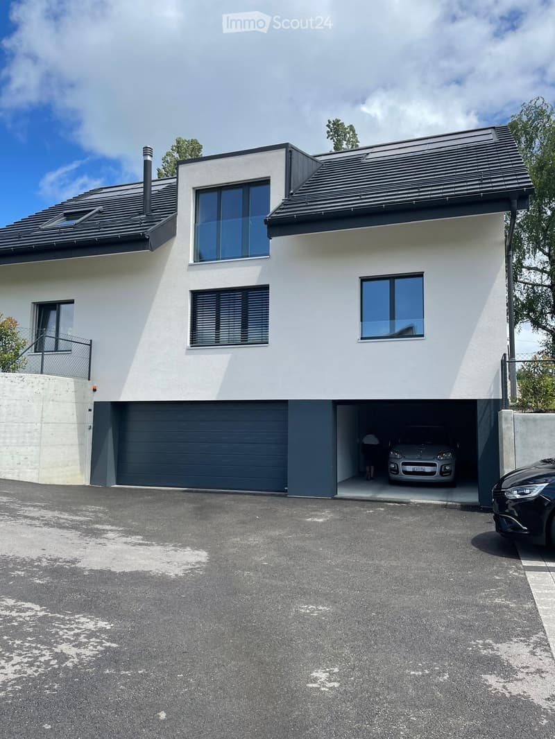 House. Modern two-story house with white exterior, dark grey roof, large windows, and a garage with an open door showing a parked car.