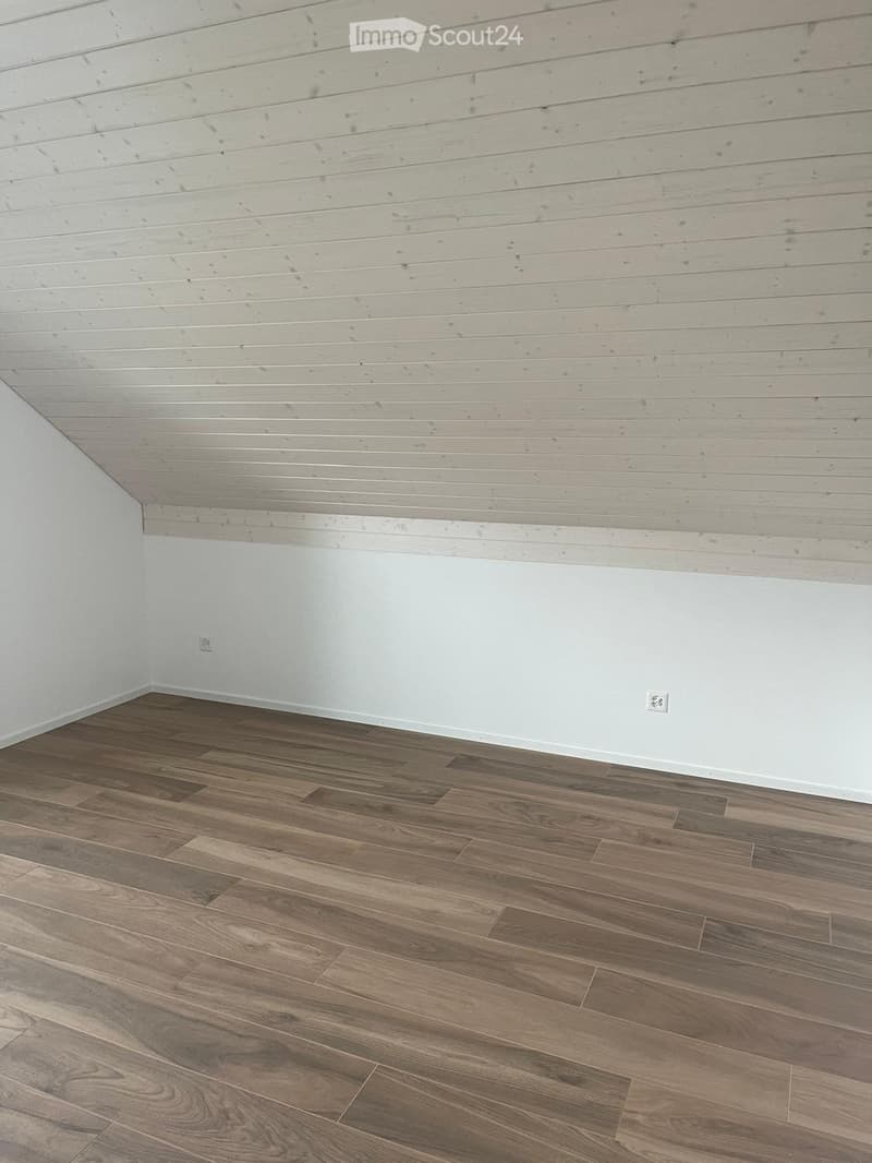 Unfurnished Room. Empty room with wooden flooring and white walls, featuring a slanted wooden ceiling and electrical outlets on the walls.