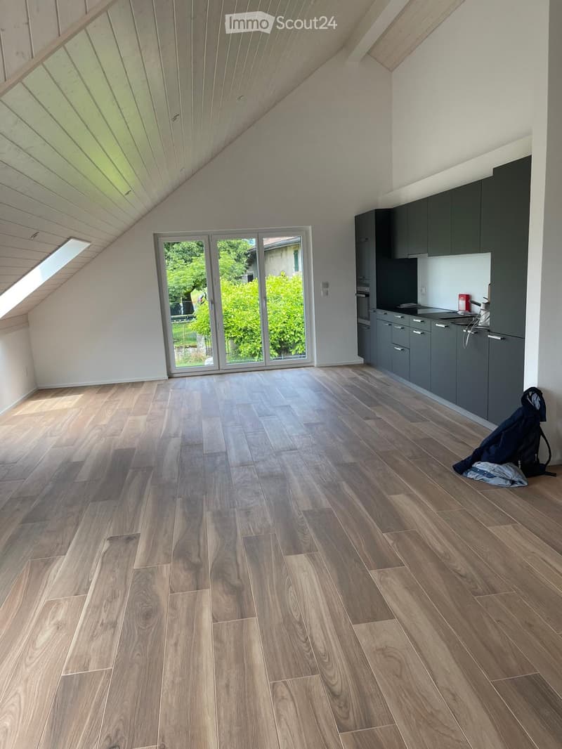 Unfurnished Room. Empty kitchen with wooden flooring, grey cabinets, and large windows overlooking a garden. No furniture or appliances are present.
