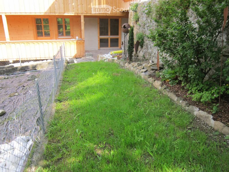 Garden / Outdoor Area. Well-maintained garden with a fenced area, stone border, and a small stream-like feature. The house in the background has wooden and stone elements with large windows and a covered entrance.