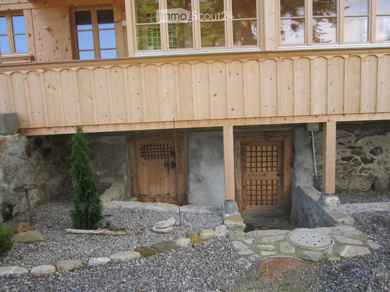 House. Two-story wooden house with large windows, stone foundation, and small garden area with gravel, rocks, and a small tree.