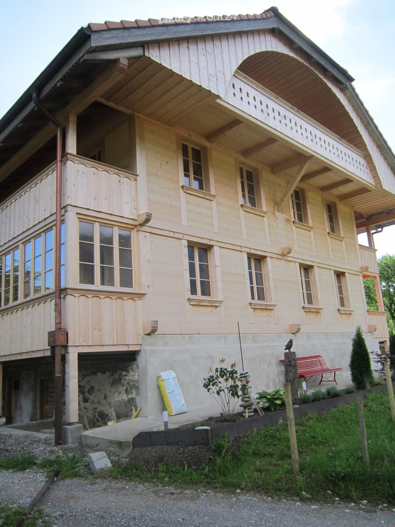 House. Two-story wooden house with multiple windows, balconies, and a small garden area with a bench and plants.